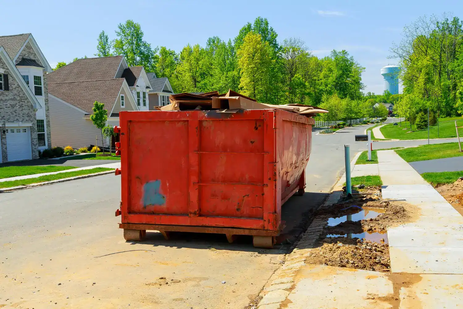 Red dumpster on street with construction debris and nearby houses.