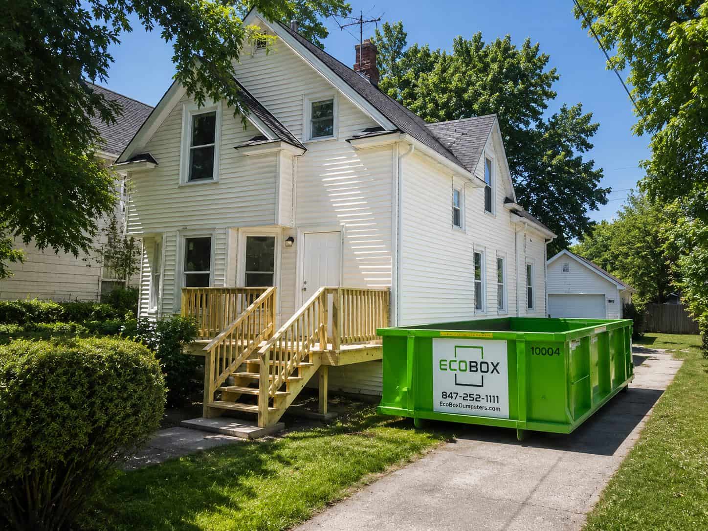 Green EcoBox dumpster placed on a suburban driveway beside a white house