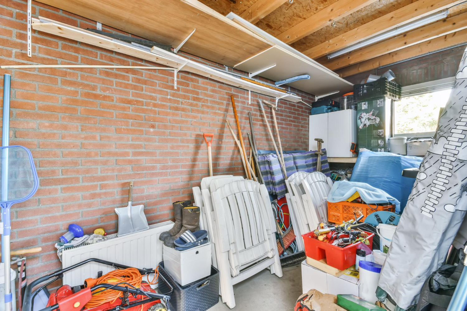 Cluttered garage interior with stacked chairs, tools, and storage boxes, illustrating the need for a residential dumpster rental for effective whole-home cleanouts.