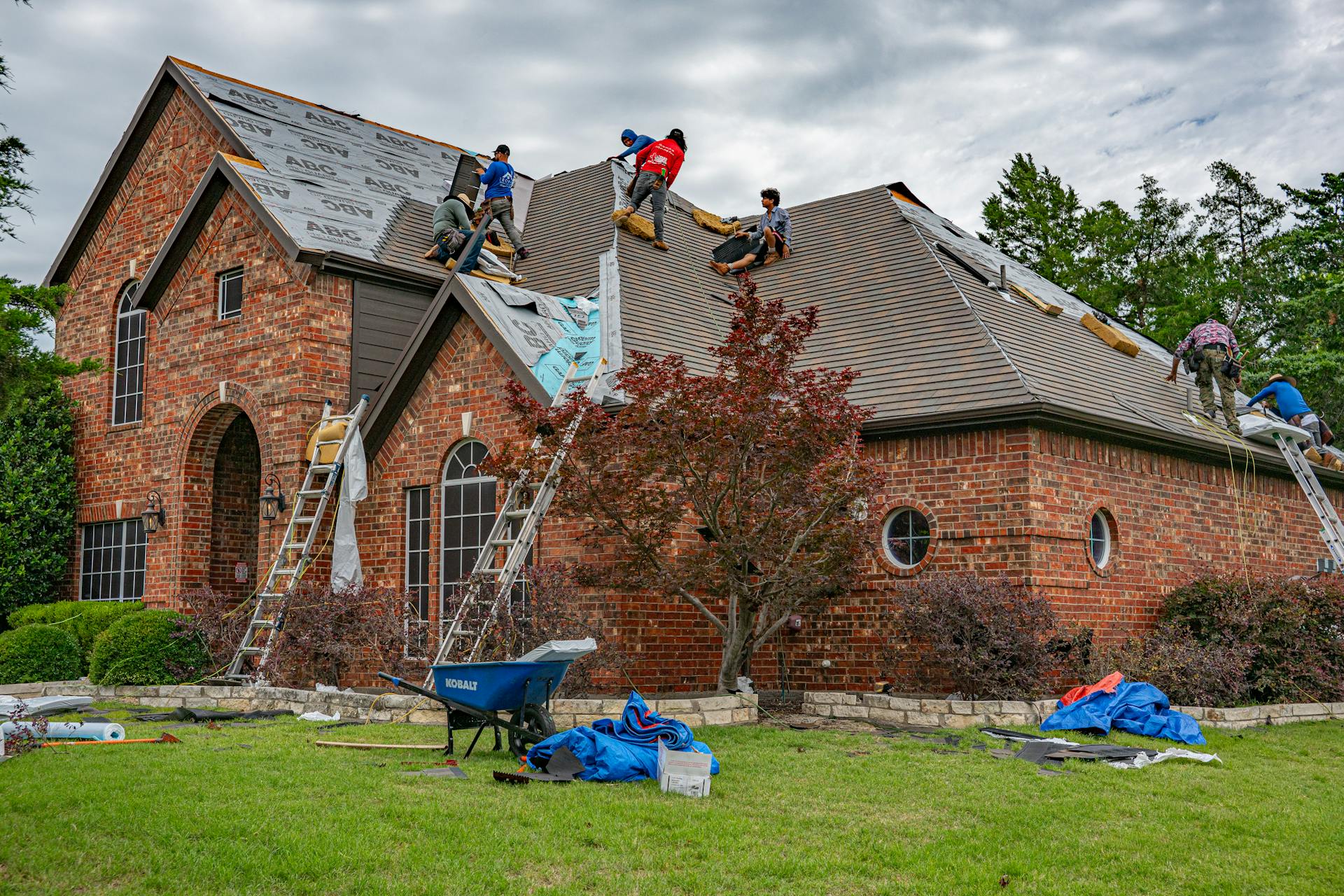 Roofing crew replacing shingles on a house in Illinois, roofing debris and wheelbarrow.