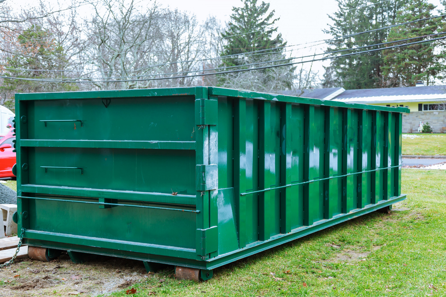 Green roll-off dumpster on grass, highlighting the importance of proper loading to avoid overloading issues during cleanup or construction projects.