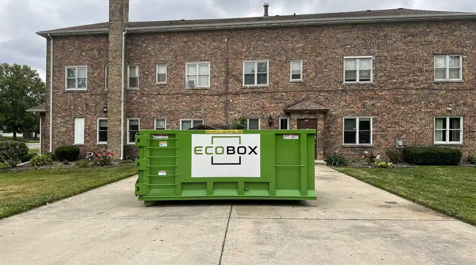 Green EcoBox dumpster placed outside a residential building for waste collection.
